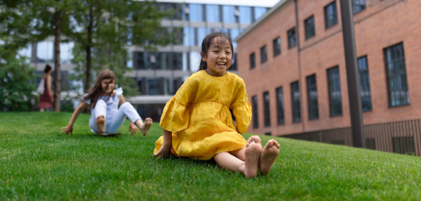 Asian girl trying to skateboarding with her friend in a city park, active kids concept. Wide photography.