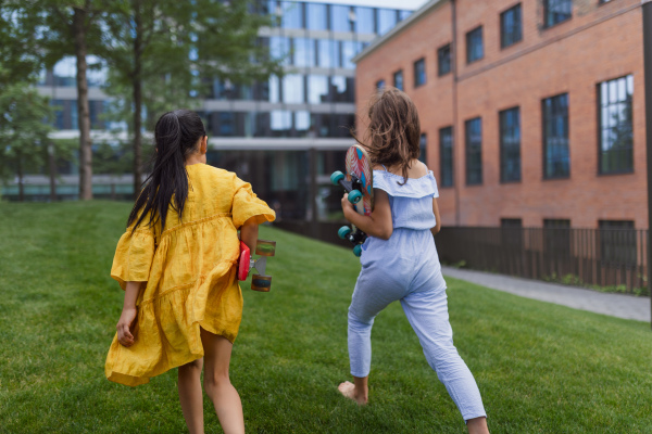 Asian girl preparing to skateboard with her friend in a city park, active kids concept. Rear view.