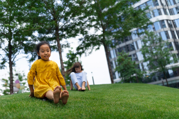 Asian girl trying to skateboarding with her friend in a city park, active kids concept. Wide photography.