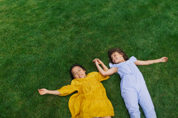 Happy girls lying in the grass, holding each other hands and having fun. Top view.