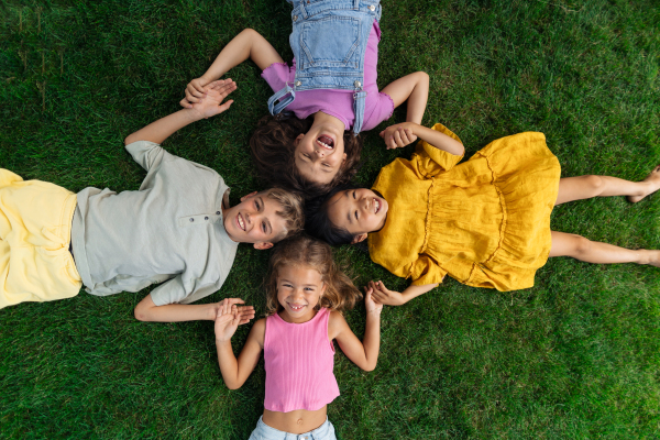 Happy four friends lying in the grass, holding each other hands and having fun. Top view.