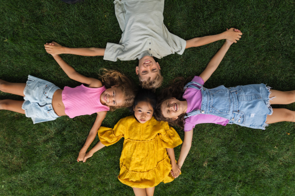 Happy four friends lying in the grass, holding each other hands and having fun. Top view.