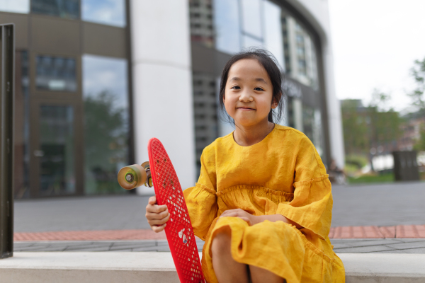 Happy asian girl with skateboard sitting outdoor in the city.