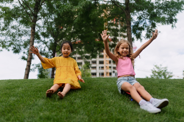 Asian girl trying to skateboarding with her friend in a city park, active kids concept.