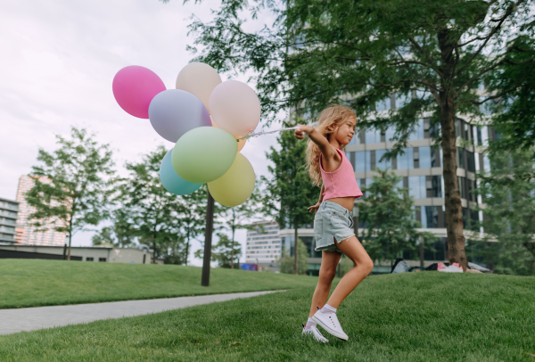 Portrait of little blond girl posing with baloons in city and looking at camera.