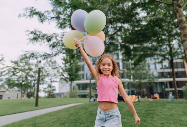 Portrait of little blond girl posing with baloons in city and looking at camera.