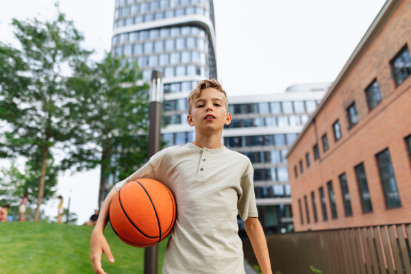 Cheerful caucasian boy with basketball ball in public city park, looking at camera.