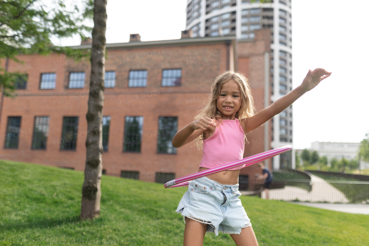 Little girl playing with hula hoop in a city park.