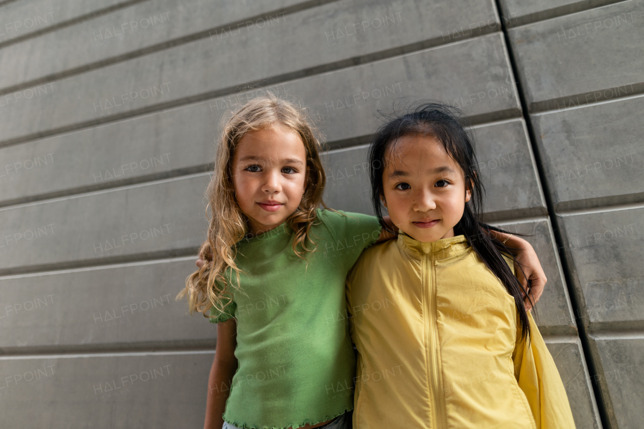 Happy friends posing together in city, standing in front of a concrete wall and looking at camera.