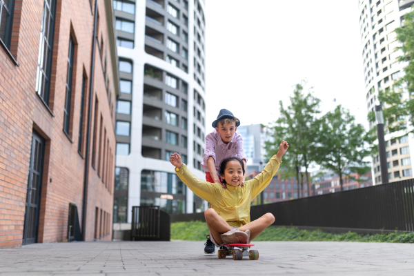 Cheerful child sitting in skateboard and going down the hill, looking at camera.