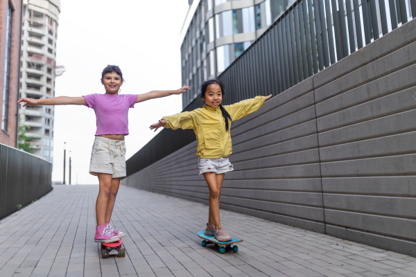 Cheerful child sitting in skateboard and going down the hill, looking at camera.