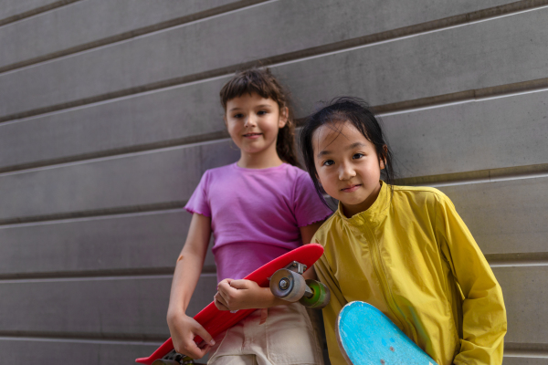 Happy friends posing together in city, standing in front of a concrete wall and looking at camera.