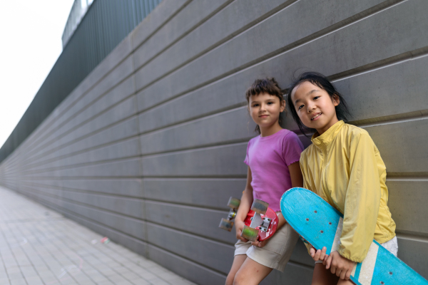 Happy friends posing together in city, standing in front of a concrete wall and looking at camera.