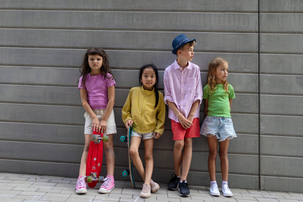 Happy friends posing together in city, standing in front of a concrete wall, holding skateboards and looking at camera.