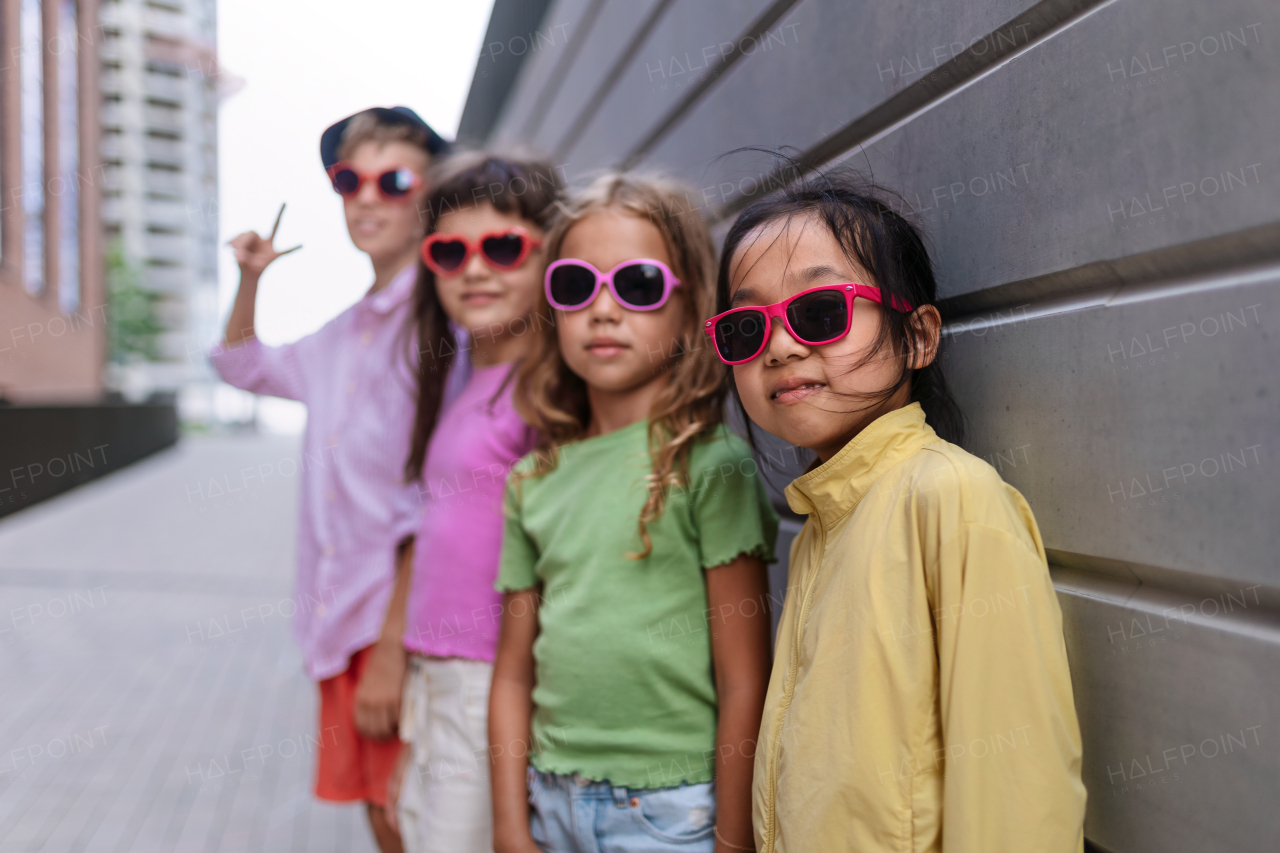 Happy friends posing together in city, standing in front of a concrete wall and looking at camera.