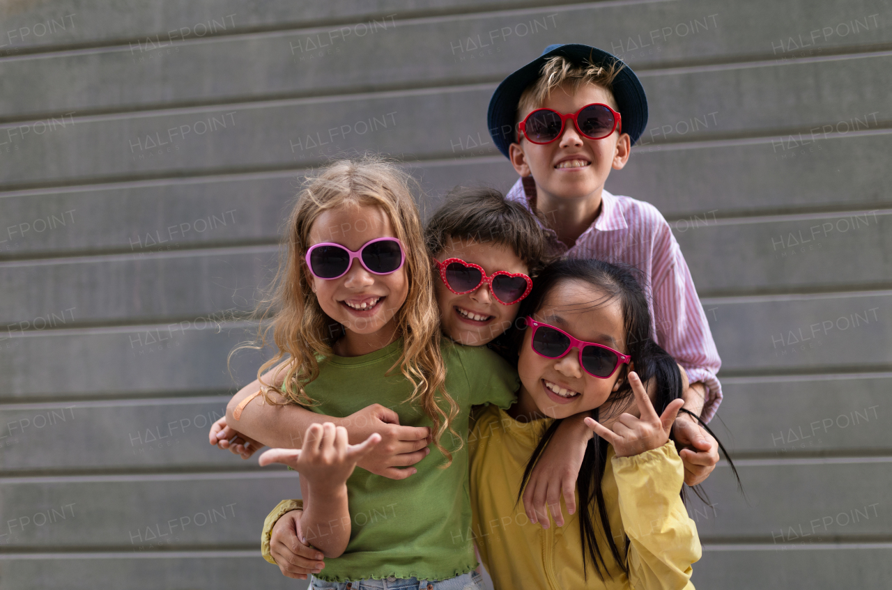 Happy friends posing together in city, standing in front of a concrete wall and looking at camera.