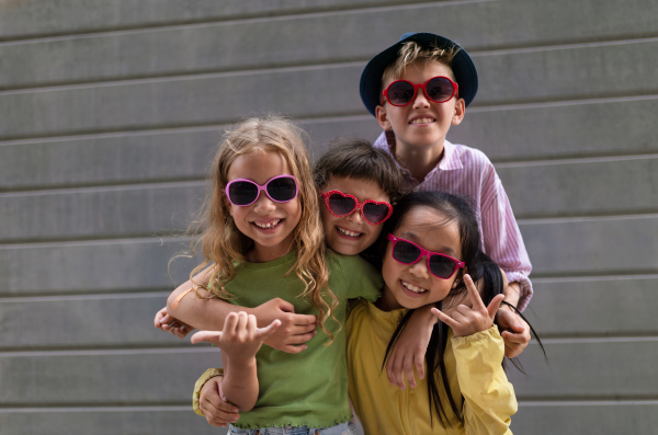 Happy friends posing together in city, standing in front of a concrete wall and looking at camera.