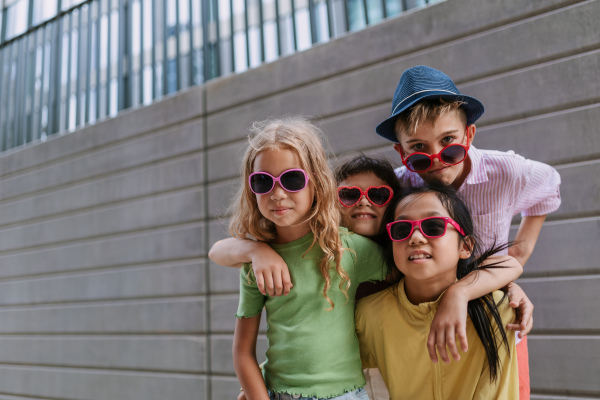 Happy friends posing together in city, standing in front of a concrete wall and looking at camera.