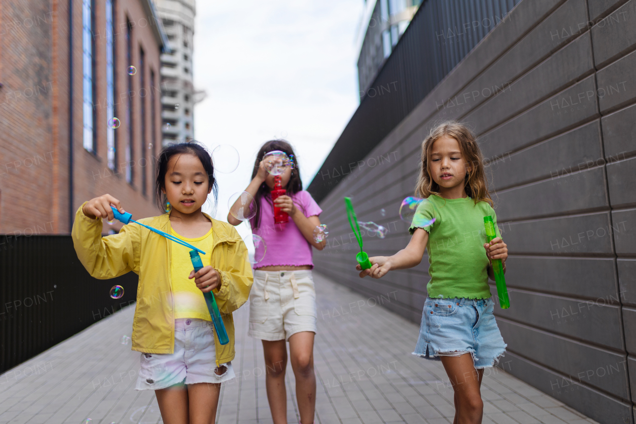 Happy three friends enjoying summer time in a city, blowing bubbles.