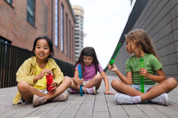 Happy three friends enjoying summer time in a city, blowing bubbles.