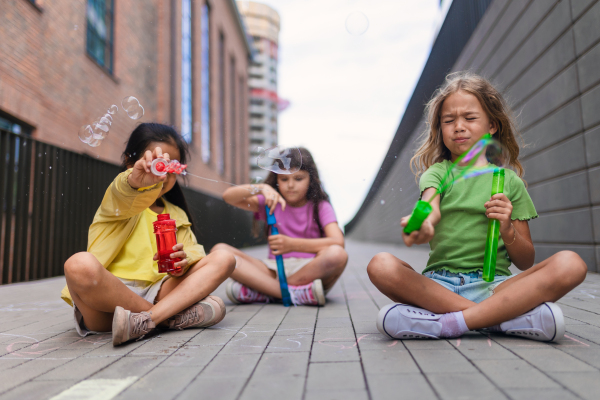 Happy three friends enjoying summer time in a city, blowing bubbles.