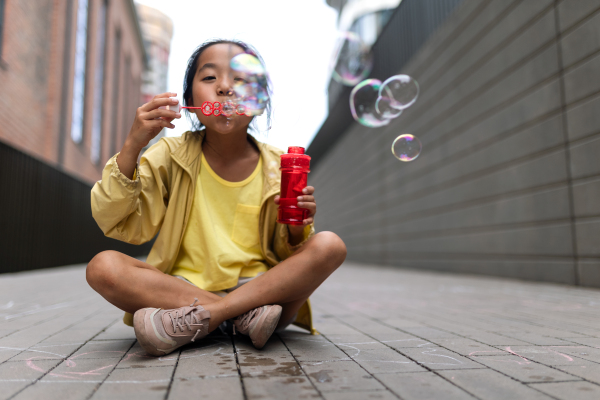 Little girl sitting in a city and blowing bubbles.