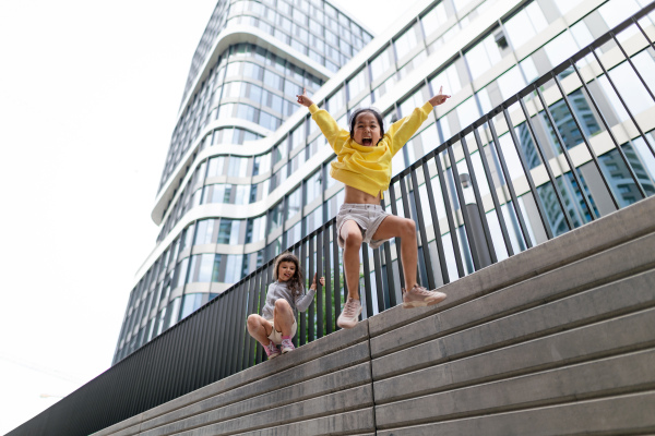 Two girls firends jumping down from concrete wall in city. Low angle view.