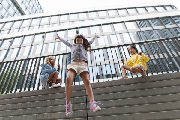 Two girls firends jumping down from concrete wall in city. Low angle view.