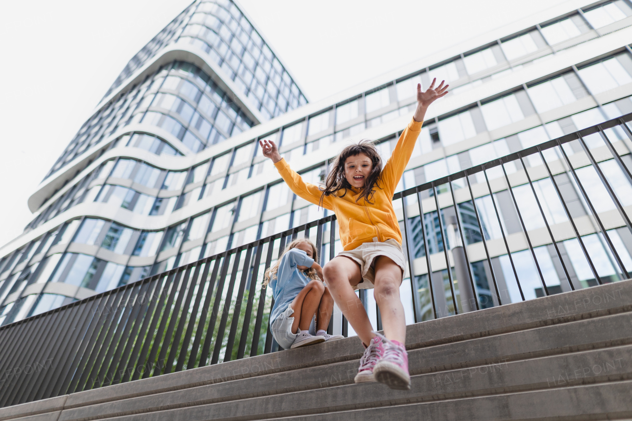 Two girls firends jumping down from concrete wall in city. Low angle view.