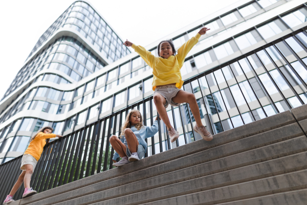 Two girls firends jumping down from concrete wall in city. Low angle view.