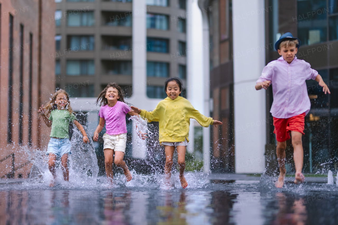 Happy four kids playing and running trough city fountain, during summer day.