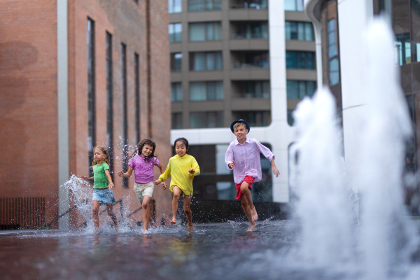 Happy four kids playing and running trough city fountain, during summer day.