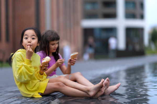 Two girls sitting, having legs in a fountain, enjoying ice cream and summer day.