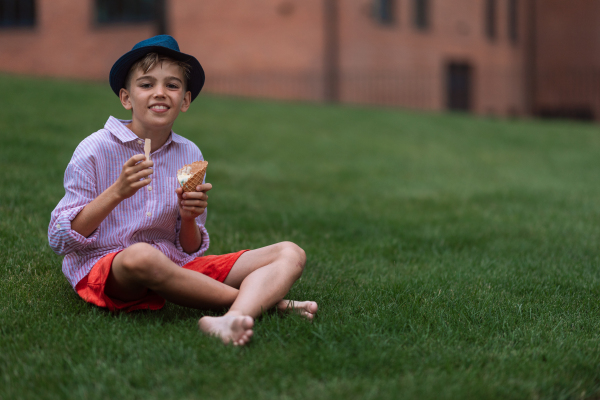 Little boy sitting in city park and eating ice cream.