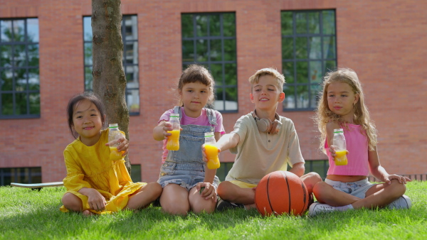 Happy kids playing and talking together in s city park, during summer day. Enjoying orange juice and looking t camera.