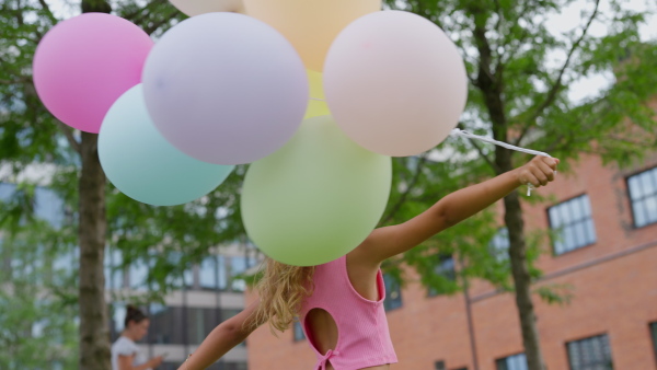 Video of little blond girl turning with baloons in city and looking at camera.