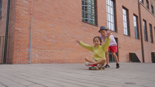 Cheerful child sitting in skateboard and going down the hill, looking at camera.