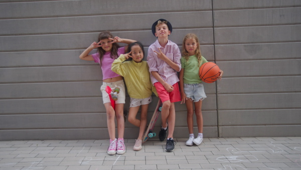 Happy friends posing together in city, standing in front of a concrete wall and looking at camera.