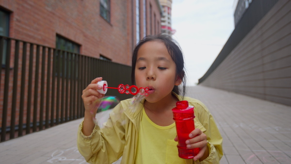 Little girl sitting in a city and blowing bubbles.