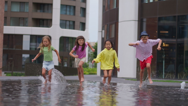 Happy four kids playing and running trough city fountain, during summer day.