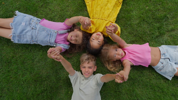 Happy four friends lying in the grass, holding each other hands and having fun. Top view.