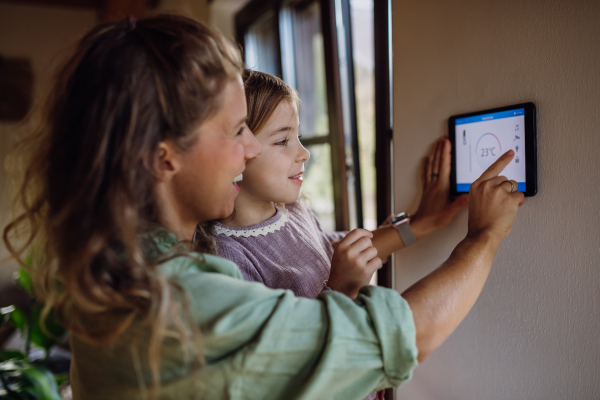 Little girl helping mother to adjust, lower heating temperature on thermostat. Concept of sustainable, efficient, and smart technology in home heating and thermostats.