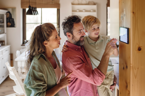 Family looking at smart thermostat, adjusting or lowering heating temperatures at home. Concept of sustainable, efficient, and smart technology in home heating and thermostats.