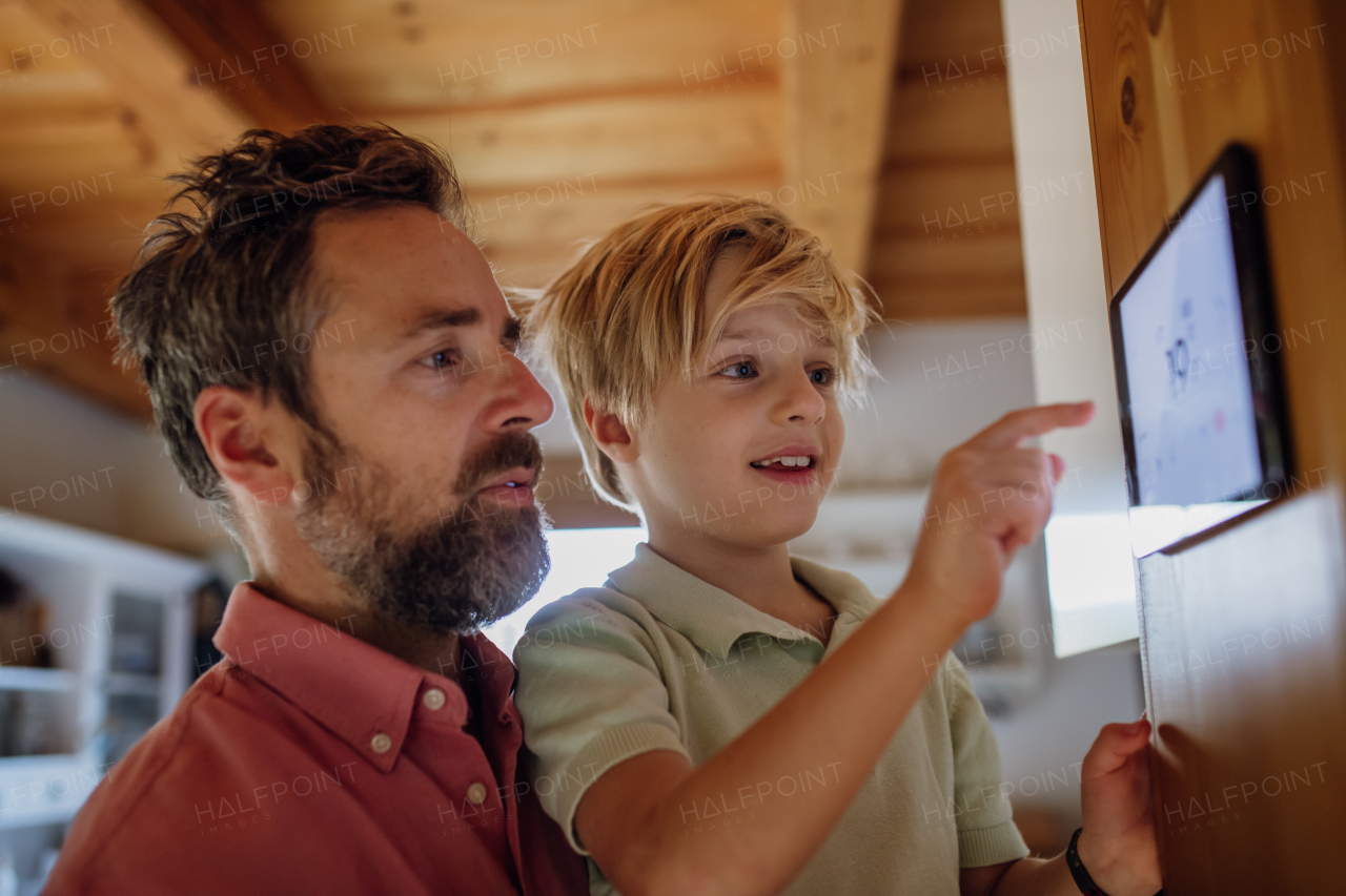 Young boy helping father to adjust, lower heating temperature on thermostat. Concept of sustainable, efficient, and smart technology in home heating and thermostats.