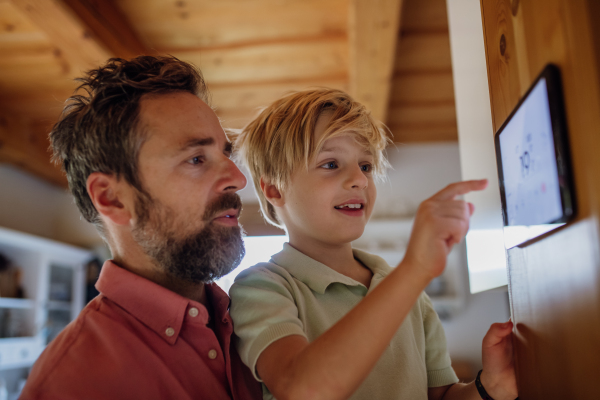 Young boy helping father to adjust, lower heating temperature on thermostat. Concept of sustainable, efficient, and smart technology in home heating and thermostats.