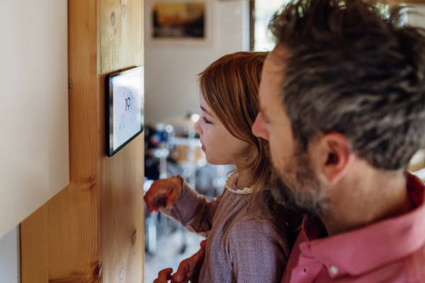 Little girl helping father to adjust, lower heating temperature on thermostat. Concept of sustainable, efficient, and smart technology in home heating and thermostats.