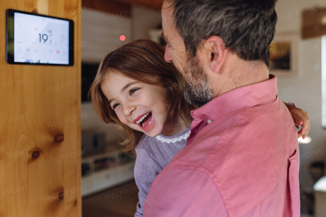 Father looking at smart thermostat, adjusting or lowering heating temperatures at home. Concept of sustainable, efficient, and smart technology in home heating and thermostats.