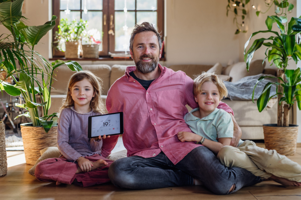 Father and two kids holding smart thermostat, adjusting or lowering heating temperatures at home. Concept of sustainable, efficient, and smart technology in home heating and thermostats.