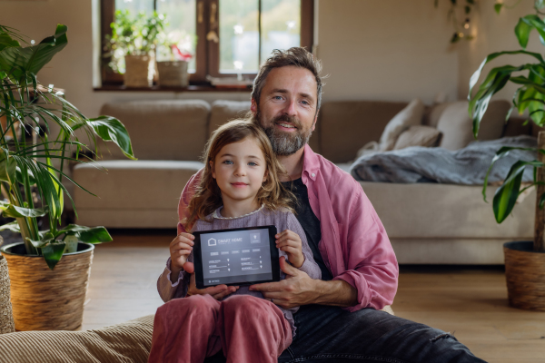 Father and little daughter holding smart thermostat, adjusting or lowering heating temperatures at home. Concept of sustainable, efficient, and smart technology in home heating and thermostats.