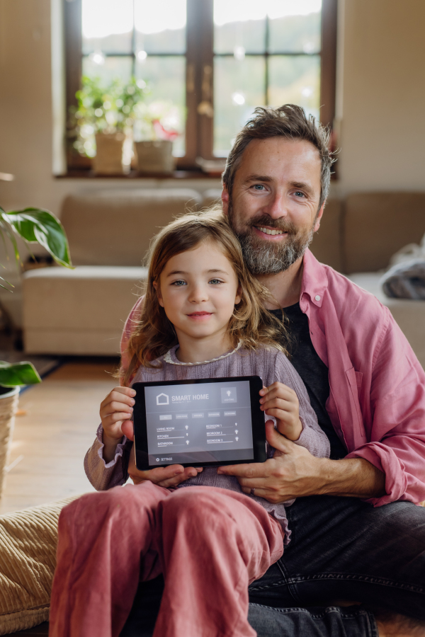 Father and little daughter holding smart thermostat, adjusting or lowering heating temperatures at home. Concept of sustainable, efficient, and smart technology in home heating and thermostats.